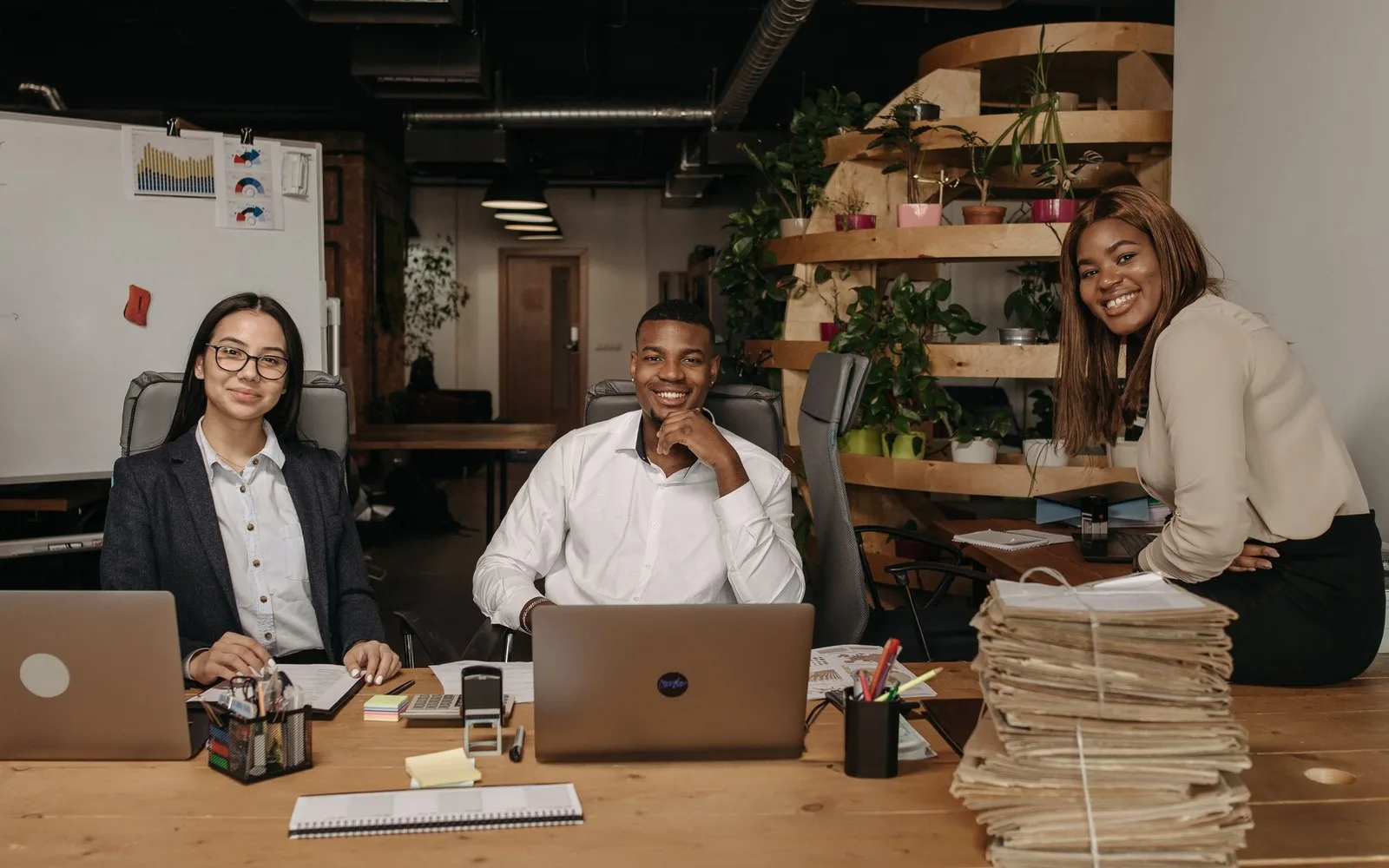 Three young professionals smiling at their desks in a bright office