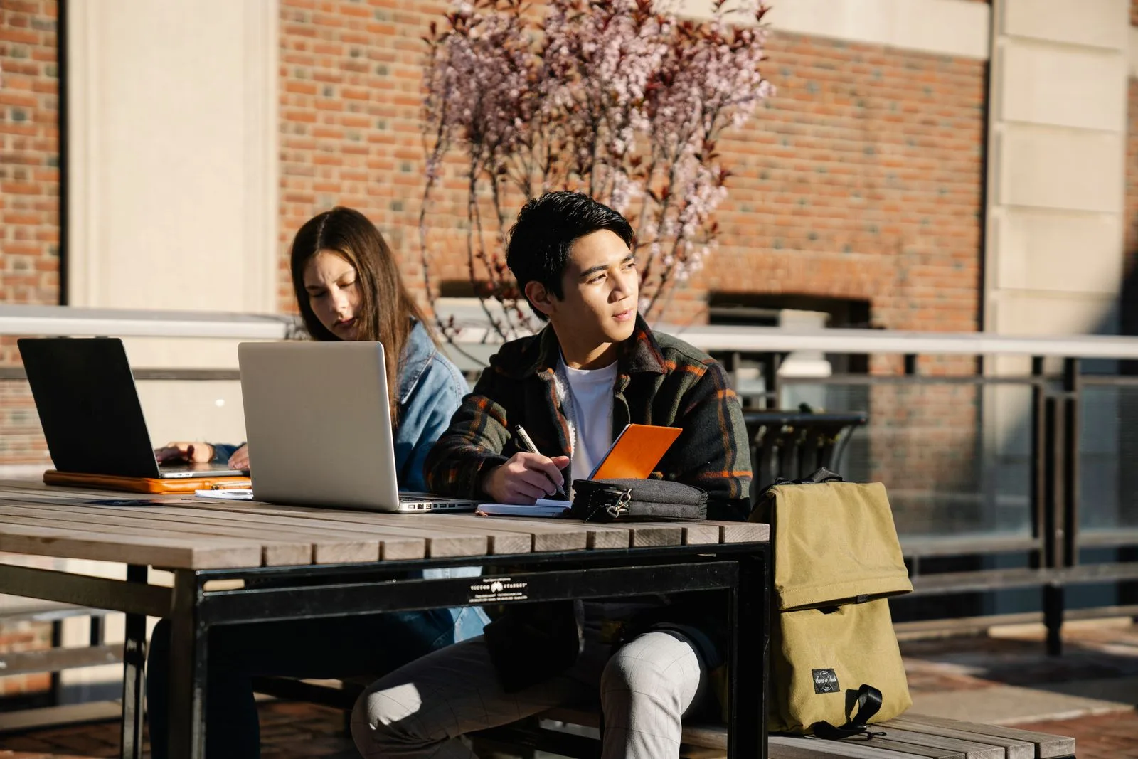 Two students working on laptops at an outdoor table