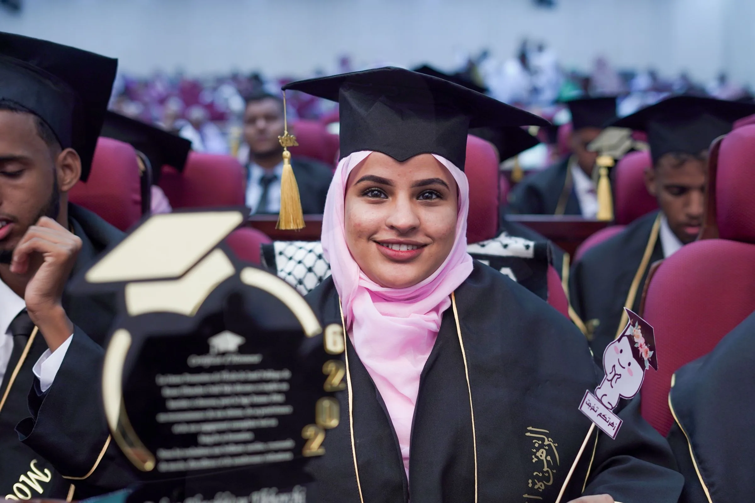 A smiling graduate in a cap and gown at a graduation ceremony