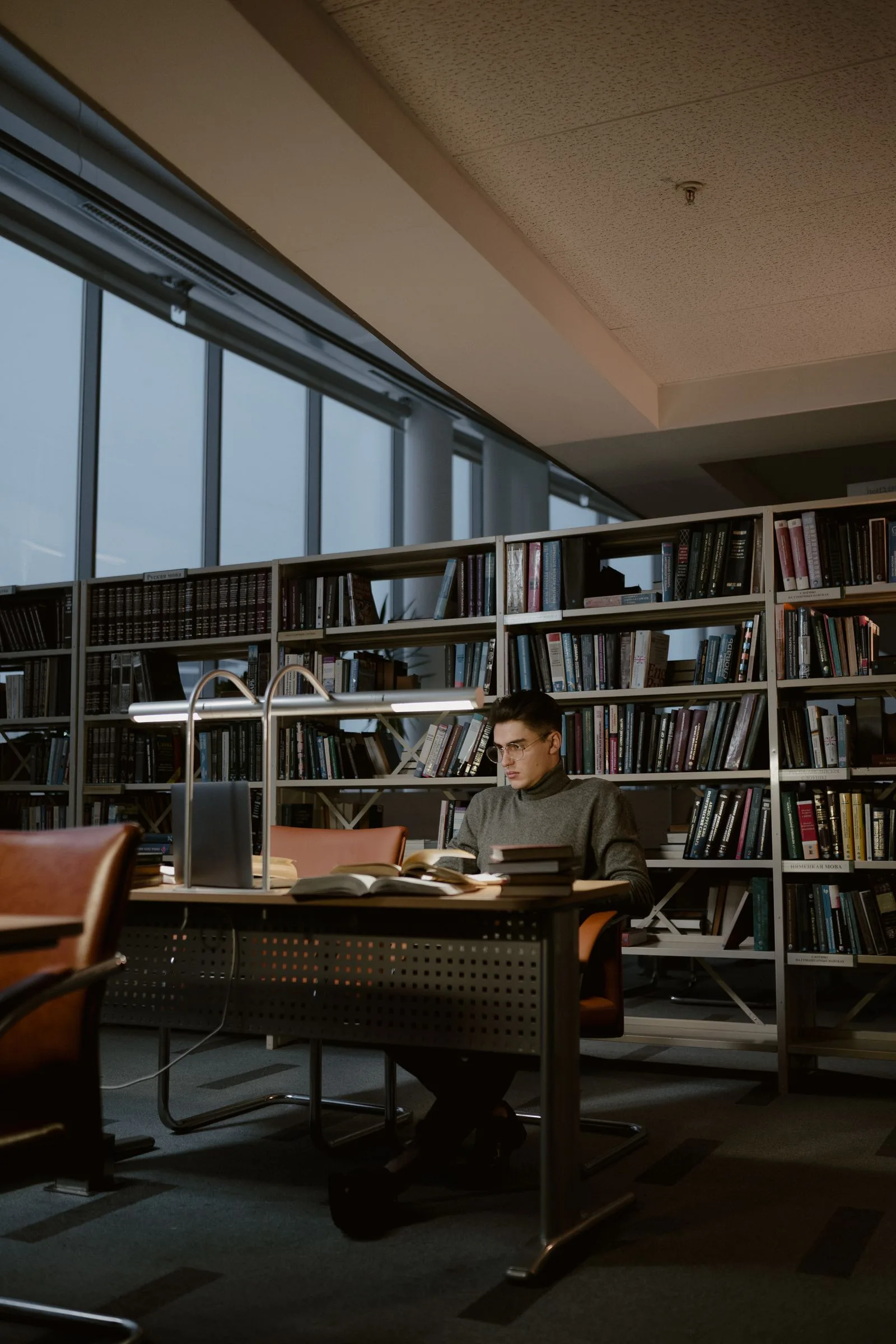 A student studying at a desk surrounded by library shelves