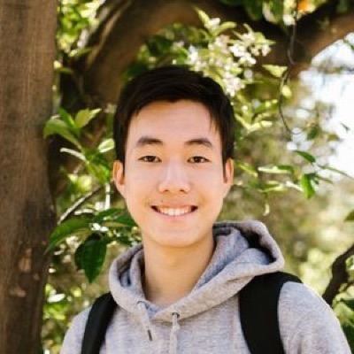 Carlo Lim, a smiling student in a grey hoodie under a tree