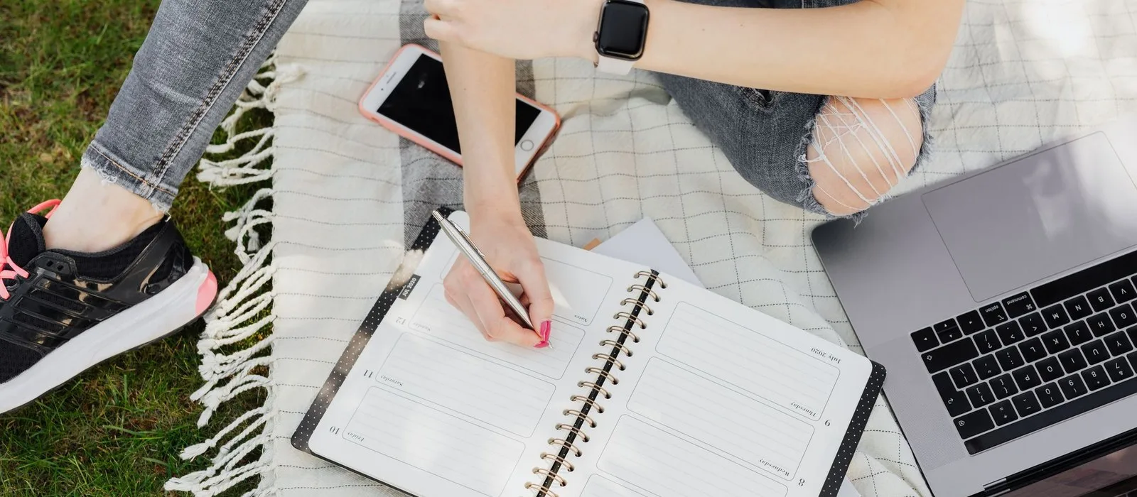 A student planning her studies in a notebook beside a laptop