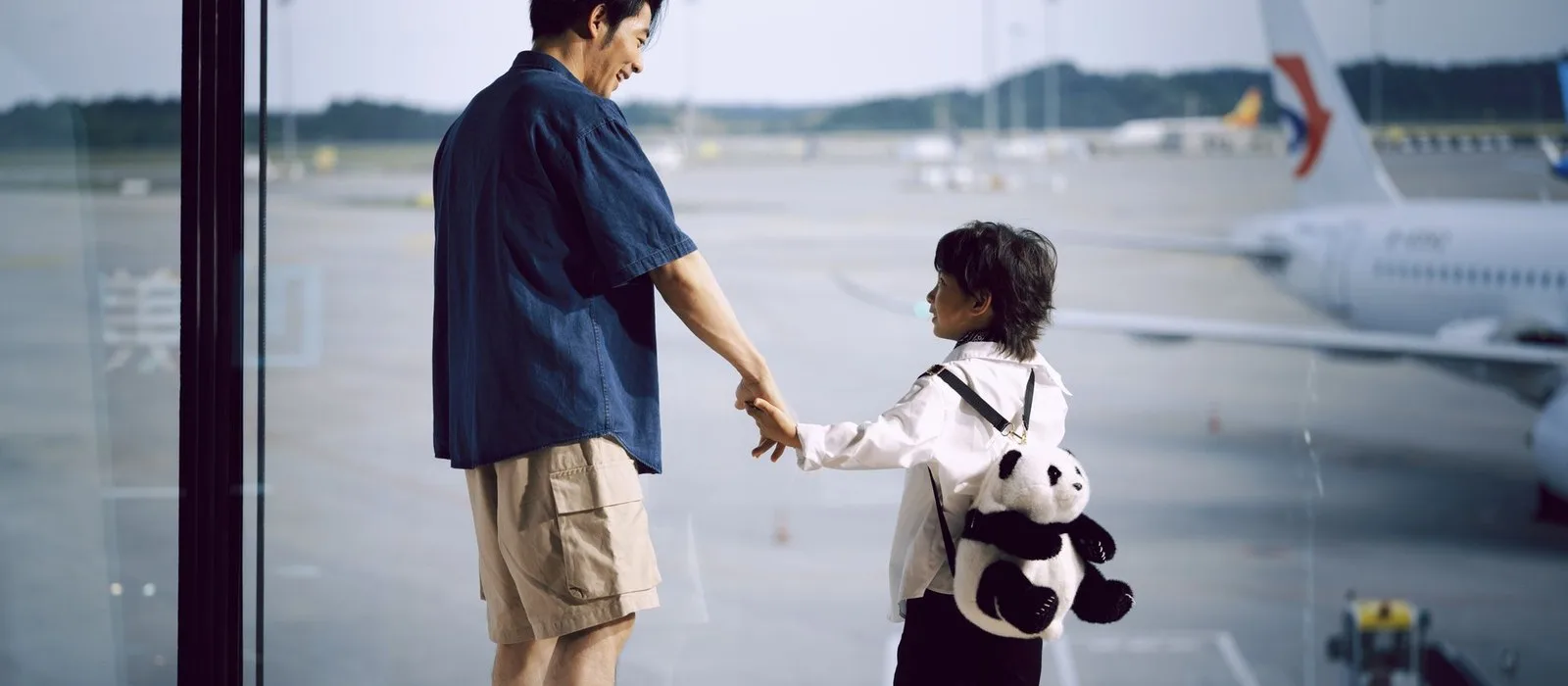 A father and child watching planes through an airport window