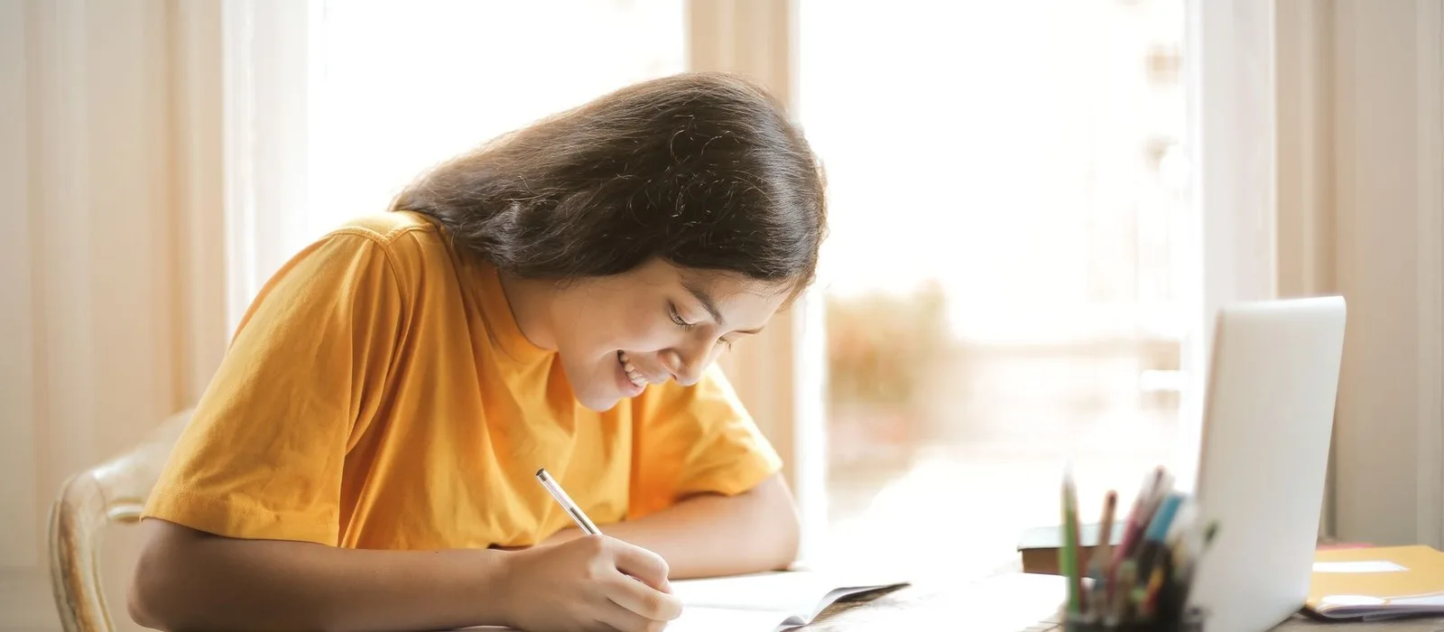 A student smiling as she writes at her desk