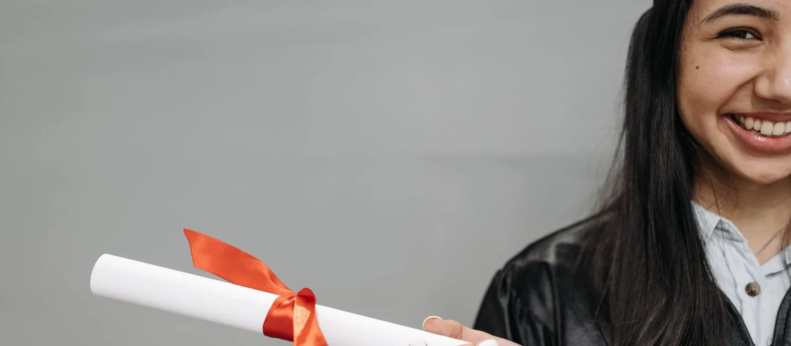 A smiling graduate holding a diploma tied with a red ribbon